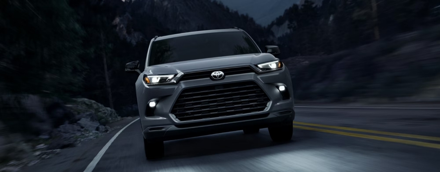 Head-on view of a grey 2025 Toyota Grand Highlander Hybrid Nightshade driving at dusk.