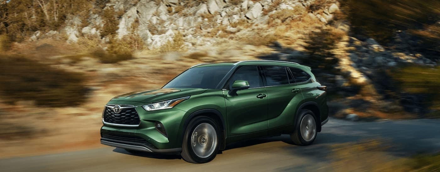 A green 2023 Toyota Highlander Hybrid driving past blurred rocks.