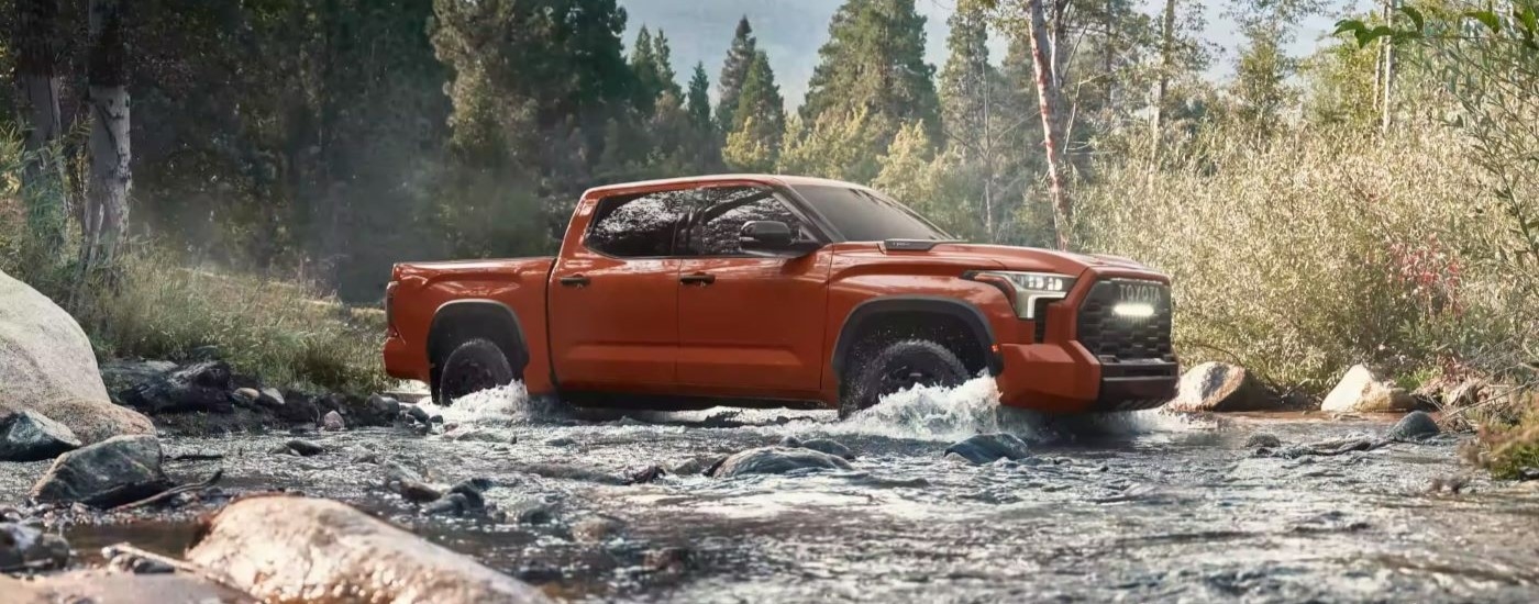 An orange 2024 Toyota Tundra TRD Pro is shown driving through a creek.