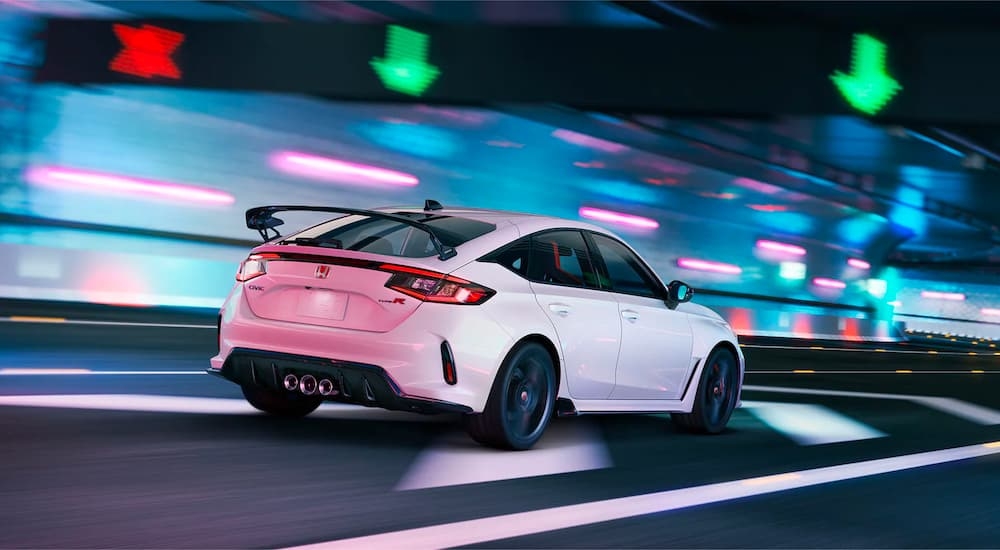 Rear view of a white 2023 Honda Civic Type R driving under neon lights.