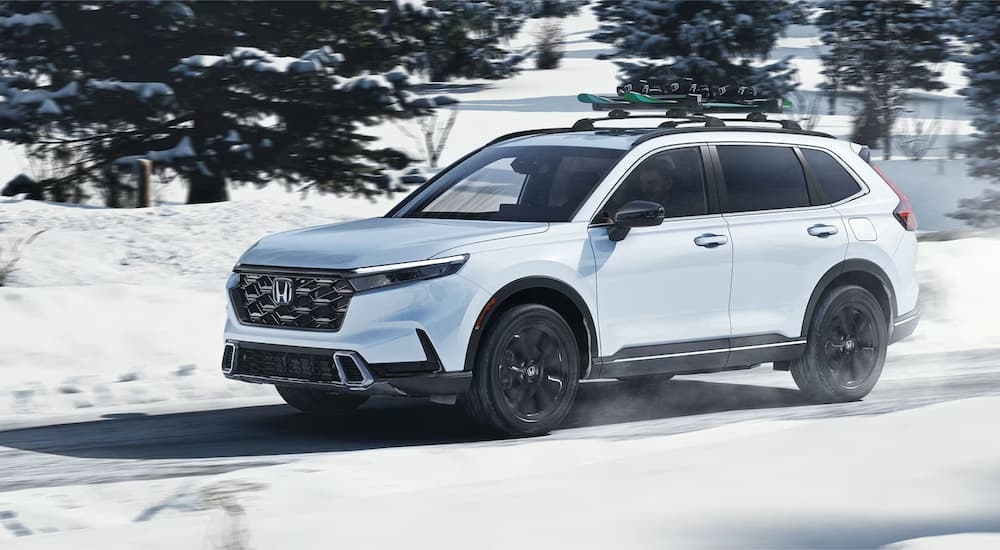 A white 2025 Honda CR-V Sport Touring Hybrid driving down a snow road.