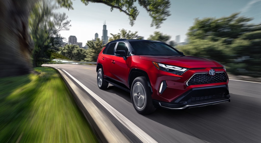 A red 2025 Toyota RAV4 PHEV driving down a road.