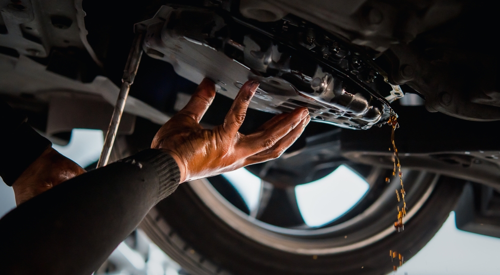 A hand holding a car transmission as it leaks fluid.