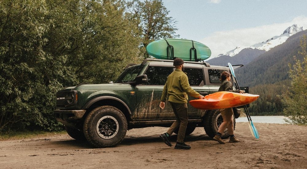 A couple unloading kayaks from a green 2025 Ford Bronco Badlands parked near water.