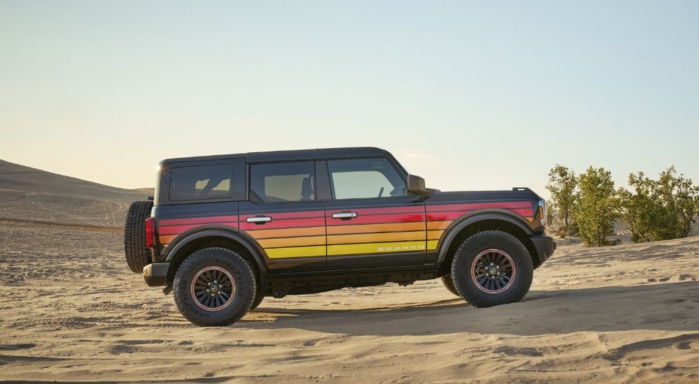 A multicolored 2025 Ford Bronco Big Bend with Free Wheeling appearance package parked on sand dunes.