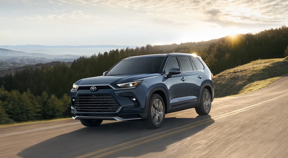 A blue 2025 Toyota Grand Highlander driving down a road.