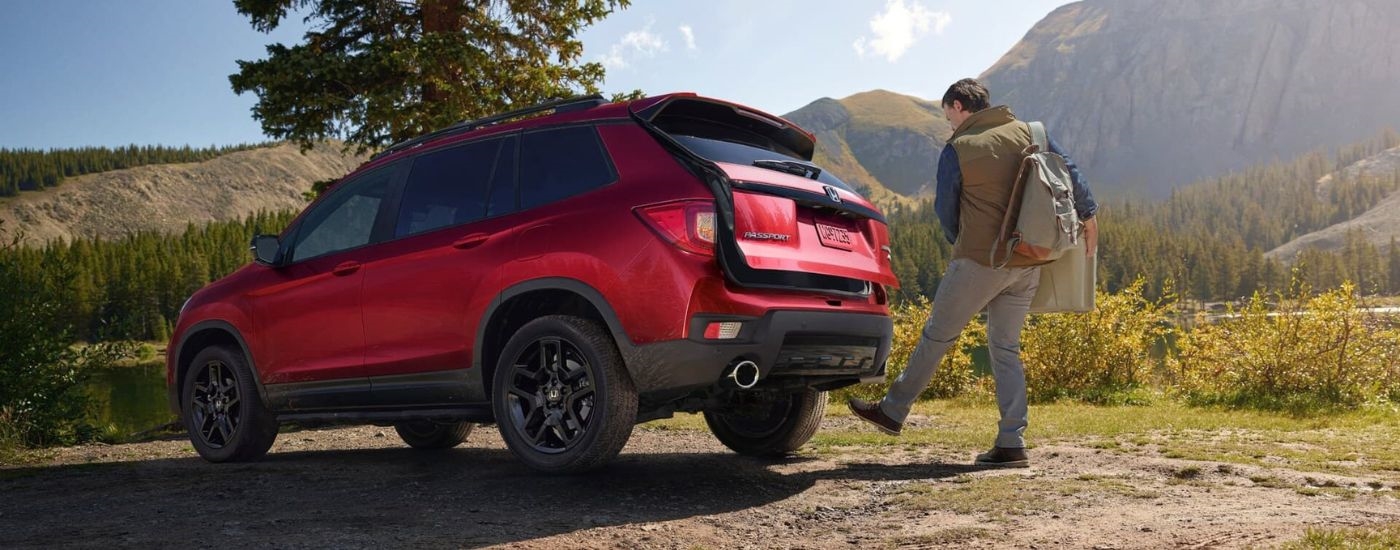 Rear view of a person opening the hatchback of a red 2024 Honda Passport.