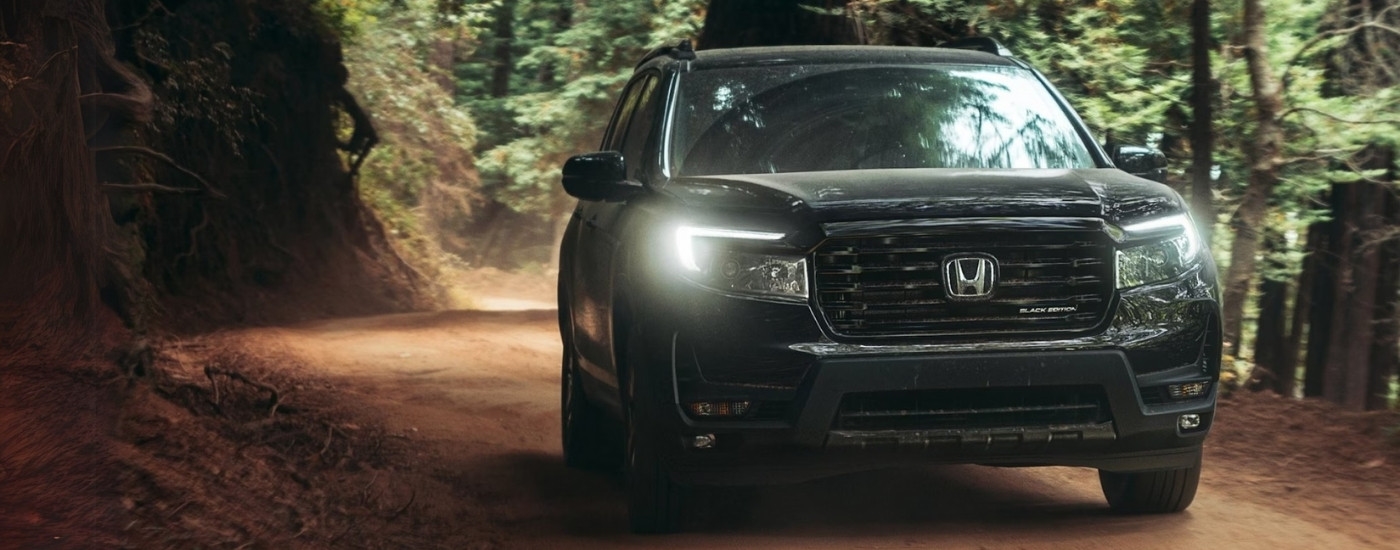 Front angle view of a black 2025 Honda Passport Black Edition driving down a dirt road.