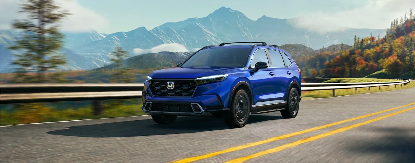 A blue 2023 Honda CR-V Hybrid Sport Touring driving around a bend.