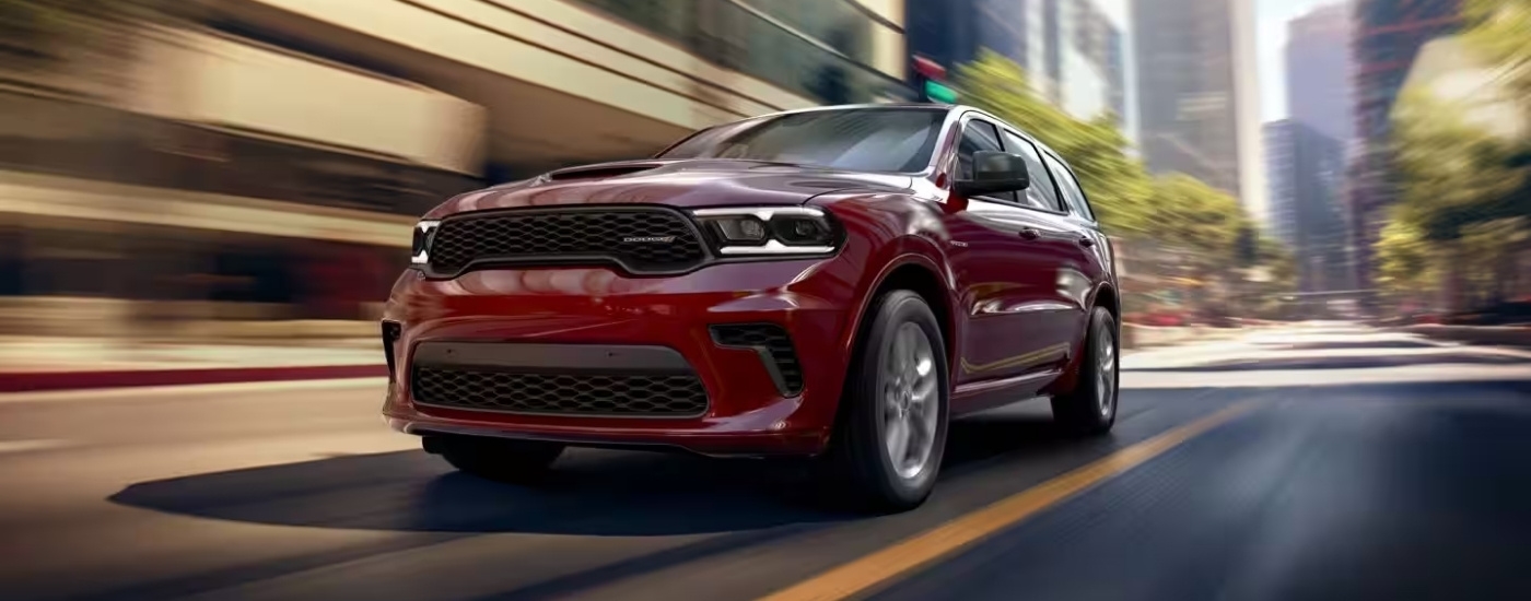 A maroon 2025 Dodge Durango is shown driving to a Dodge dealer near you.