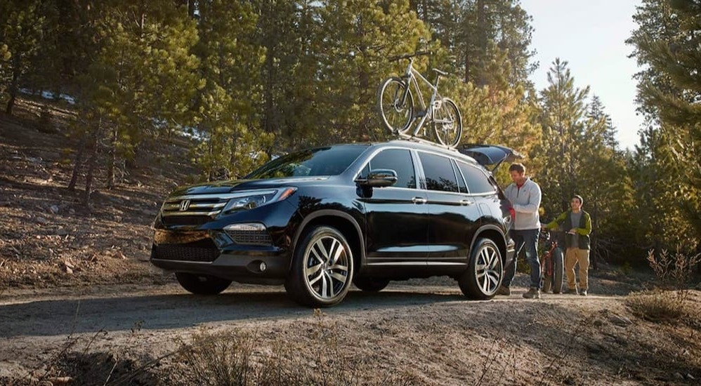 A black 2016 Honda Pilot with bicycles mounted on its roof parked off-road on a trail.