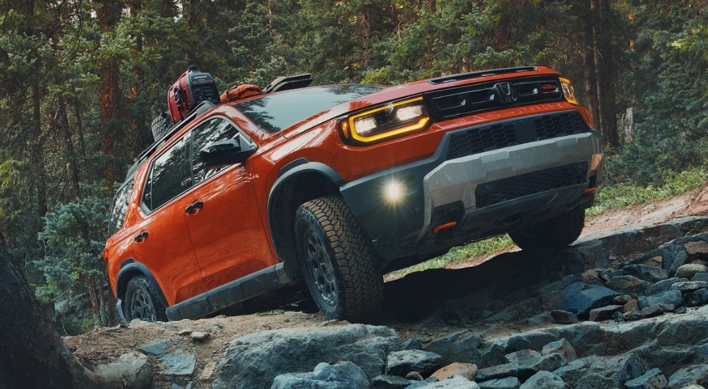 An orange 2026 Honda Passport TrailSport Elite is shown off-roading on a trail.