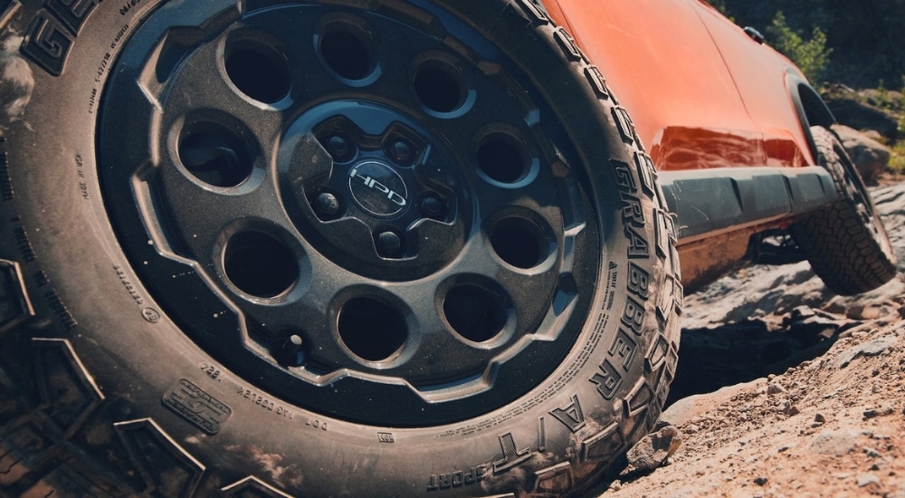 A close-up shows a black wheel on an orange 2026 Honda Passport TrailSport Elite HPD.