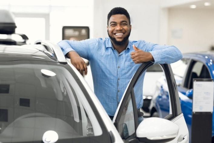 Man gesturing thumbs-up, approving automobile after test drive in dealership.