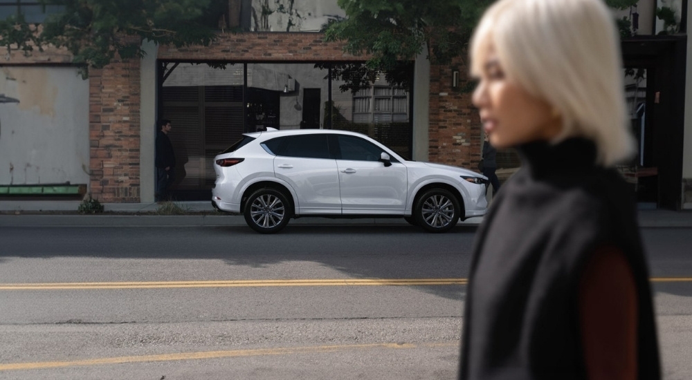 A white 2025 Mazda CX-5 is shown from the side on a city street.