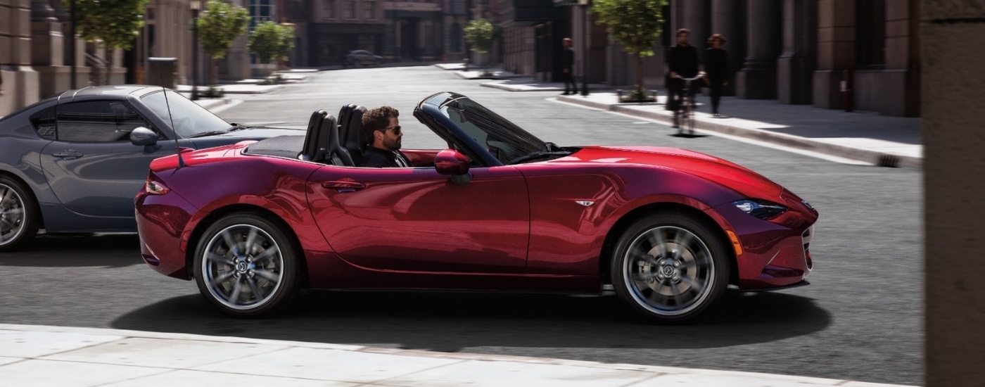 A red 2021 Mazda MX-5 Miata is driving in a city.