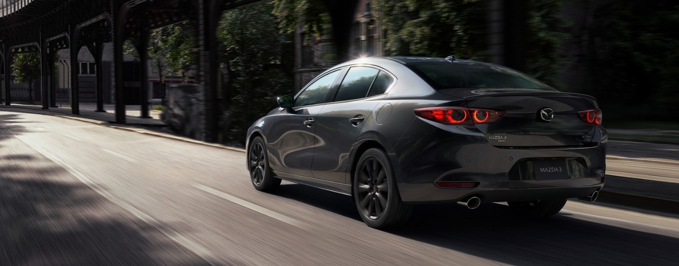 A grey 2021 Mazda3 is driving down an empty street.