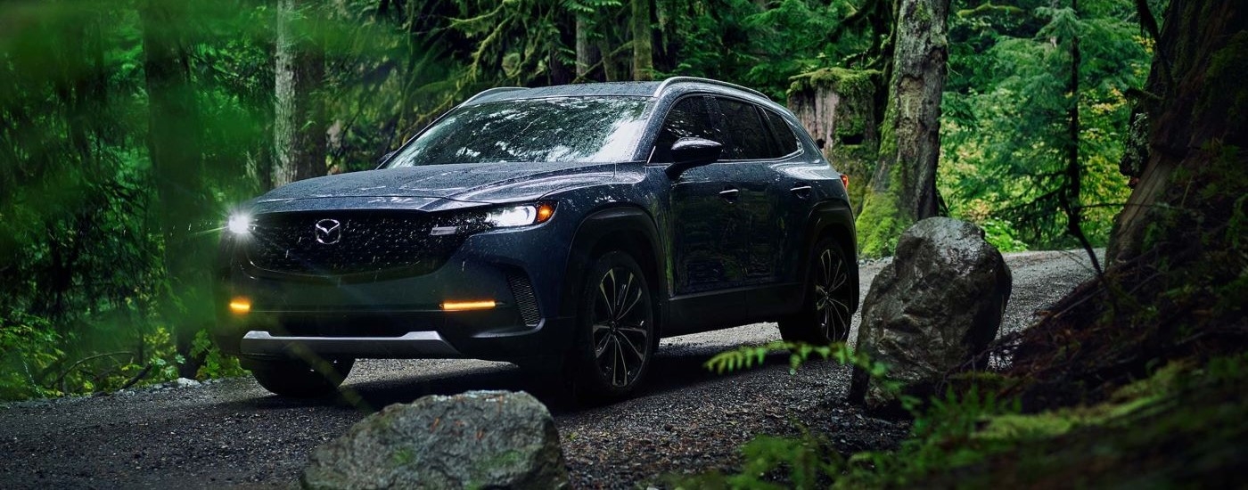 A grey 2023 Mazda CX-50 is parked off-road in a forest.