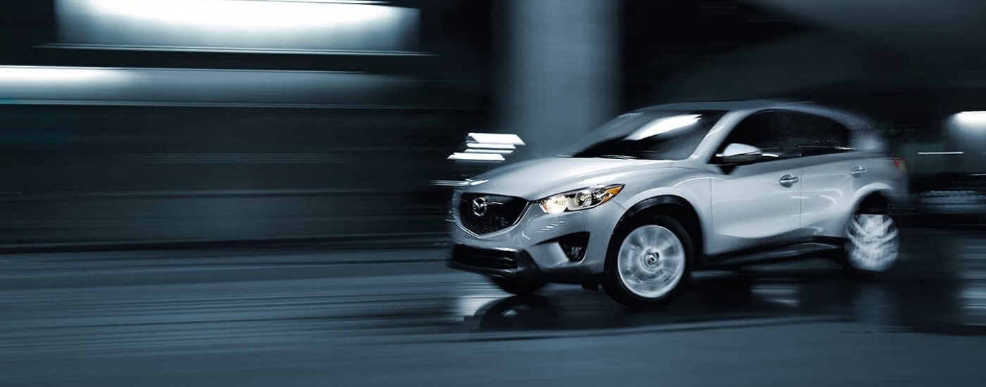 A silver 2015 Mazda CX-5 is shown driving though a parking garage.