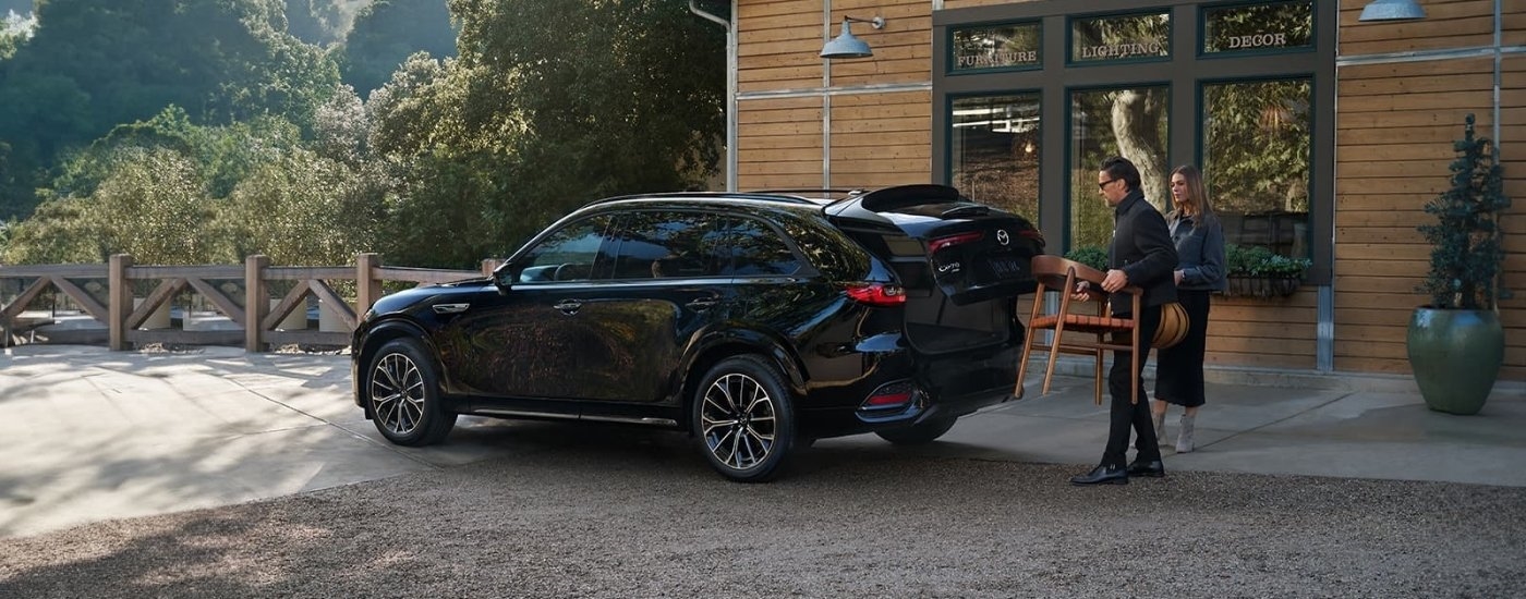 A black 2025 Mazda CX-70 for sale is outside of a furniture shop.