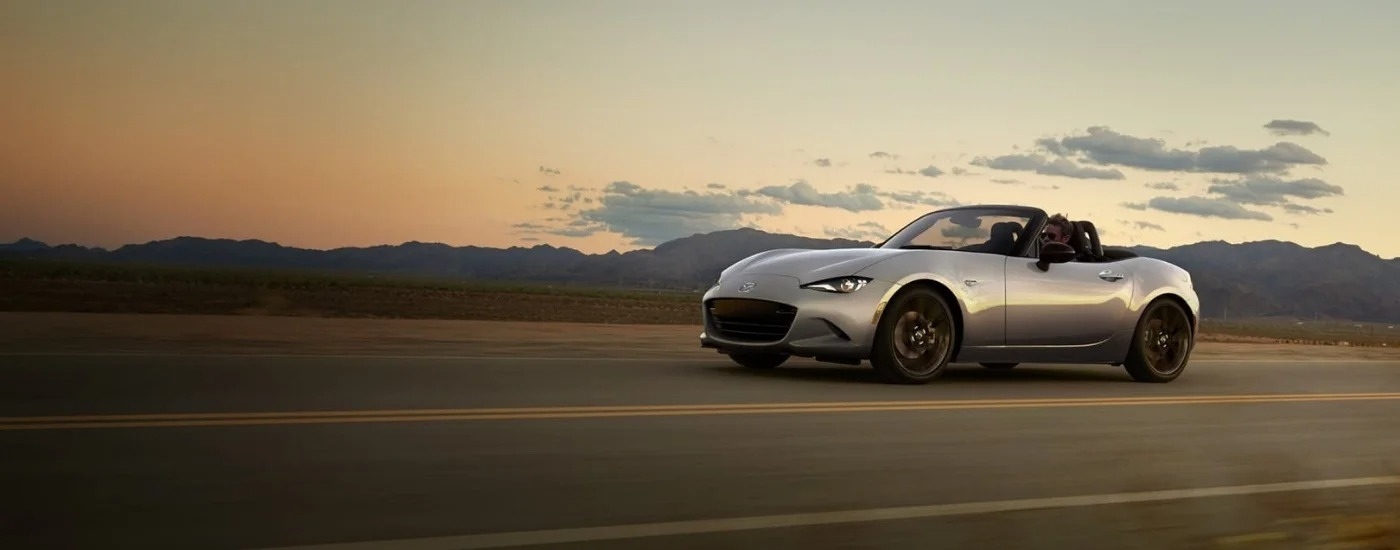 A silver 2024 Mazda MX-5 Miata is shown driving to a Mazda dealer near Spring.