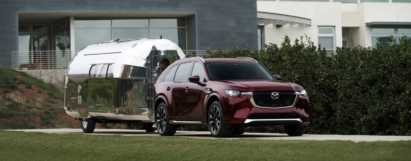 A maroon 2025 Mazda CX-90 for sale is shown towing an Airstream trailer.
