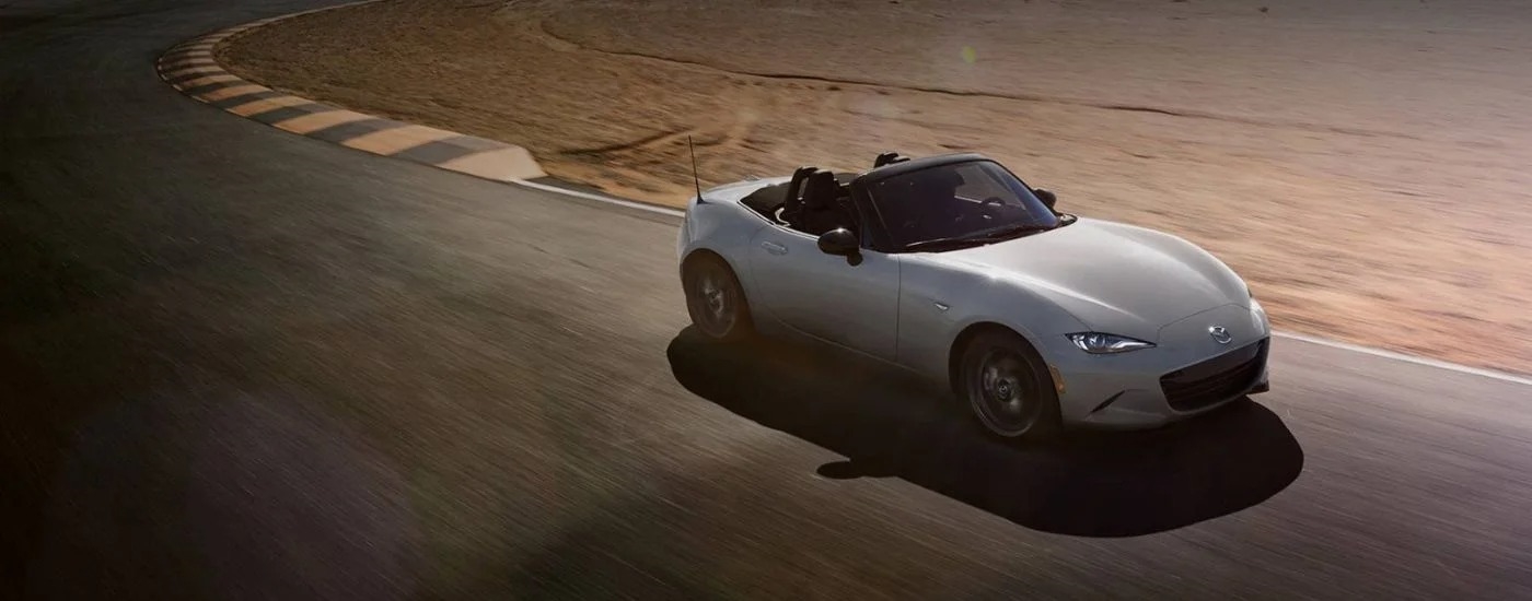 A white 2024 Mazda MX-5 Miata is shown driving on a race track.