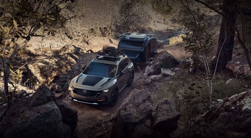 A green 2025 Mazda CX-50 towing a camper down a dirt road.