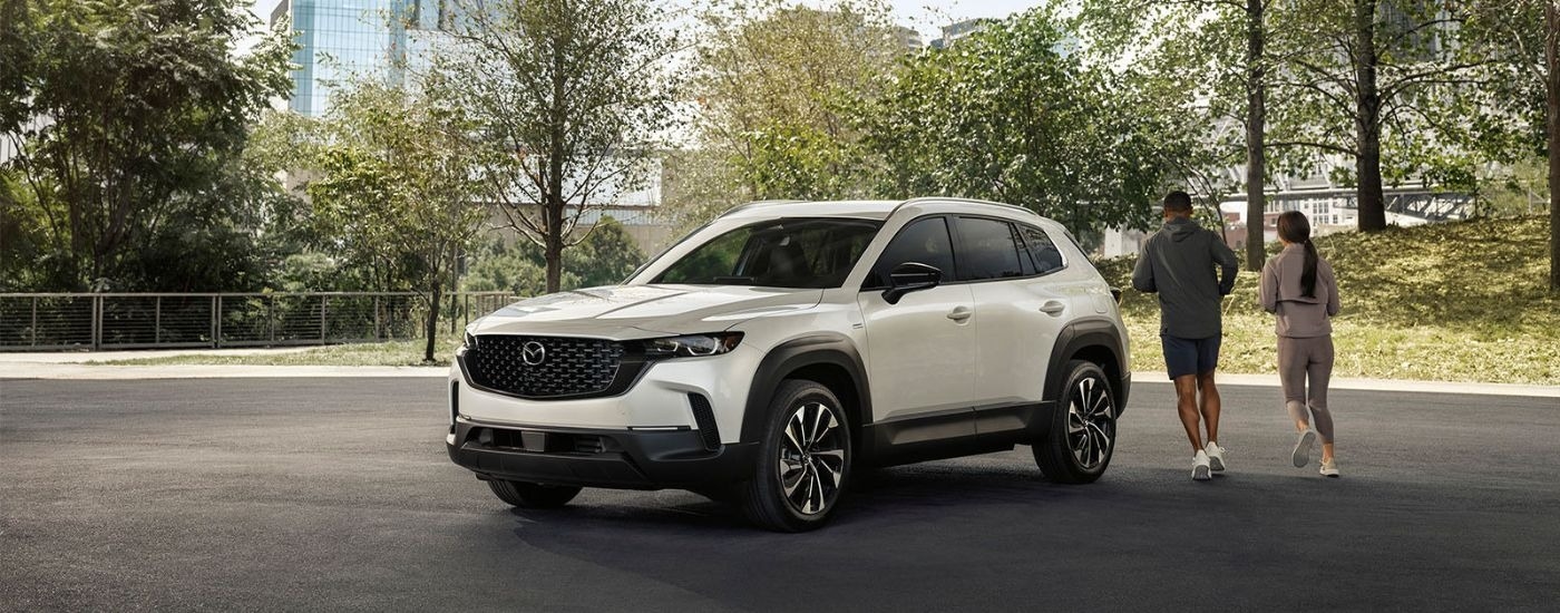 A white 2025 Mazda CX-50 parked in a city park with people jogging past.