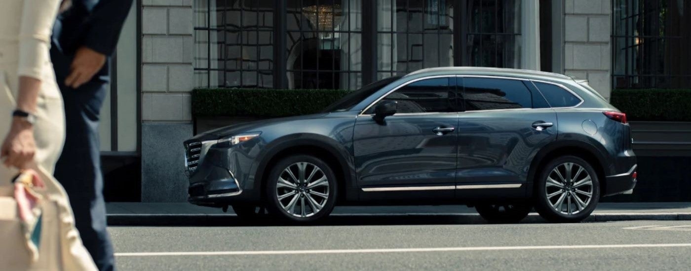 Side view of a grey-blue 2024 Mazda CX-9 parked on the side of a street.