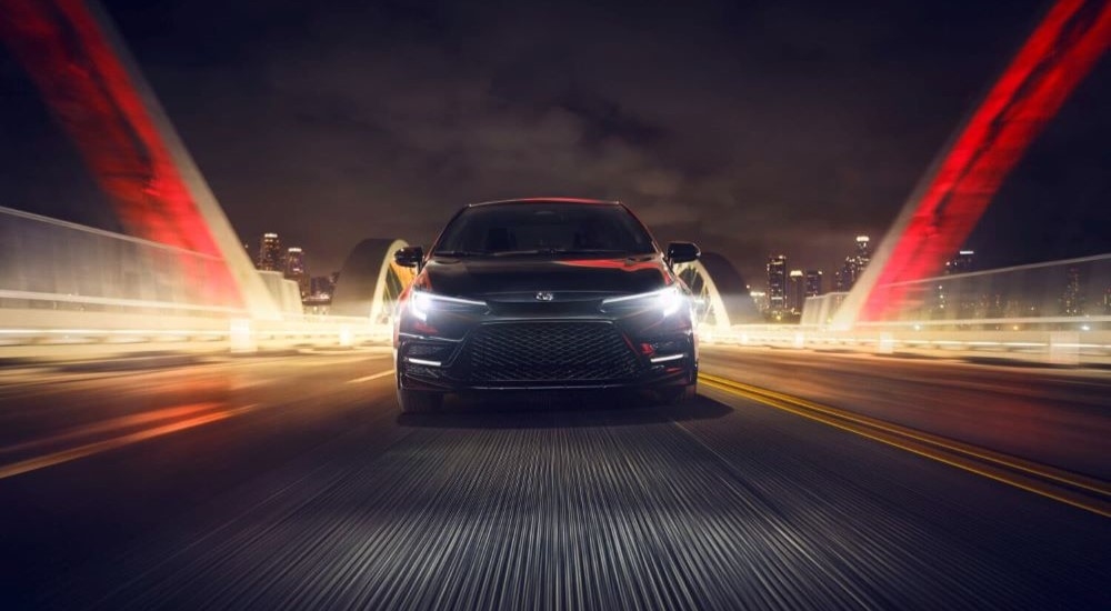 Front view of a black 2025 Toyota Corolla for sale driving down a bridge.