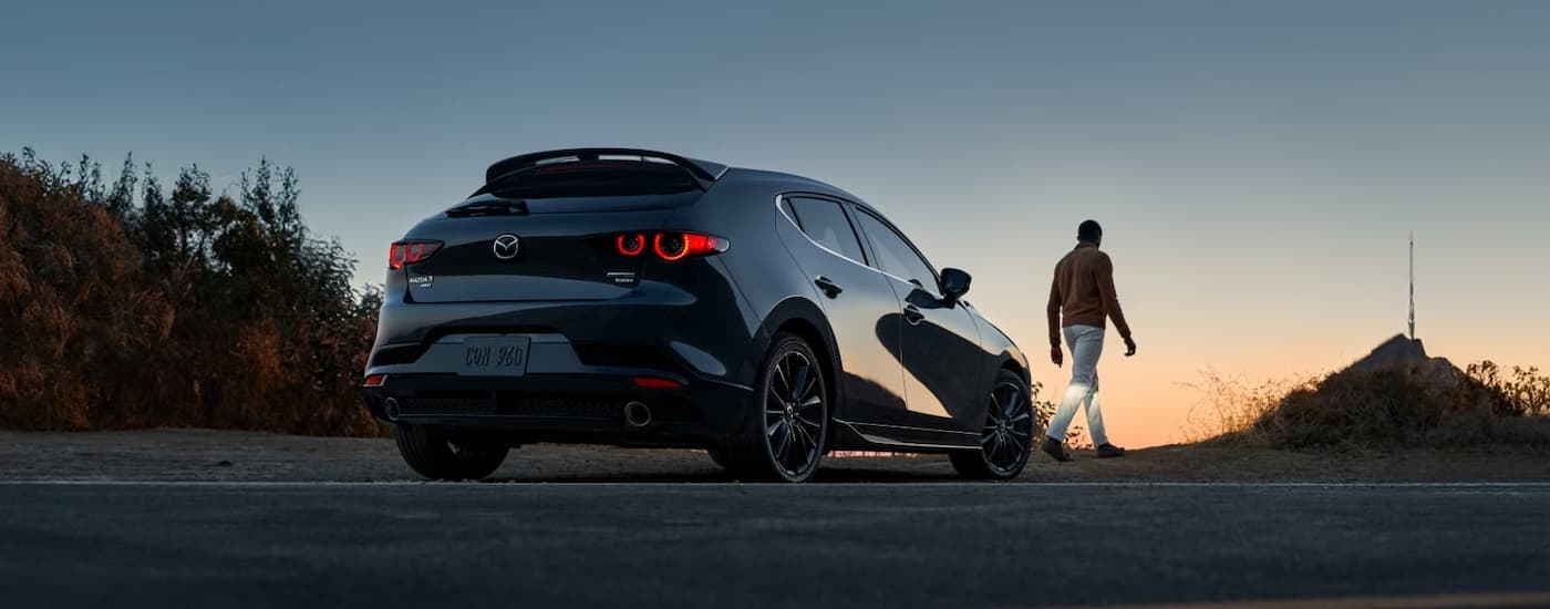 A black 2025 Mazda 3 Hatchback parked on gravel during a sunset.