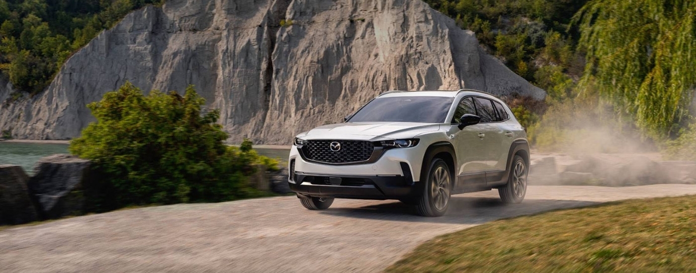 A white 2025 Mazda CX-50 Hybrid driving to a Mazda dealer.