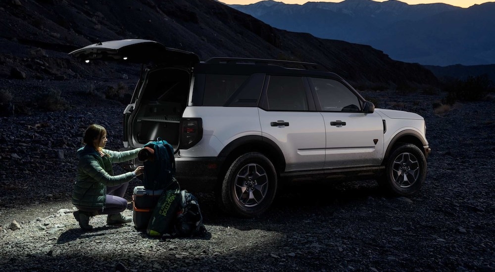 A woman kneeling near a white 2025 Ford Bronco Sport with an open hatchback.
