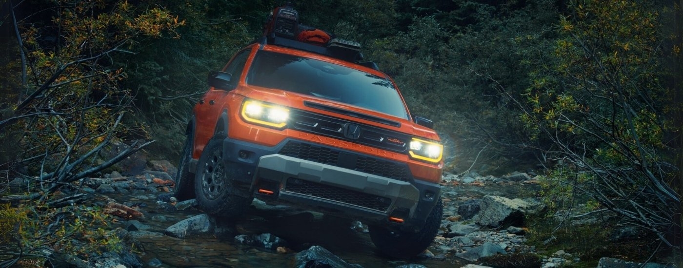 An orange 2026 Honda Passport TrailSport is parked off-road.