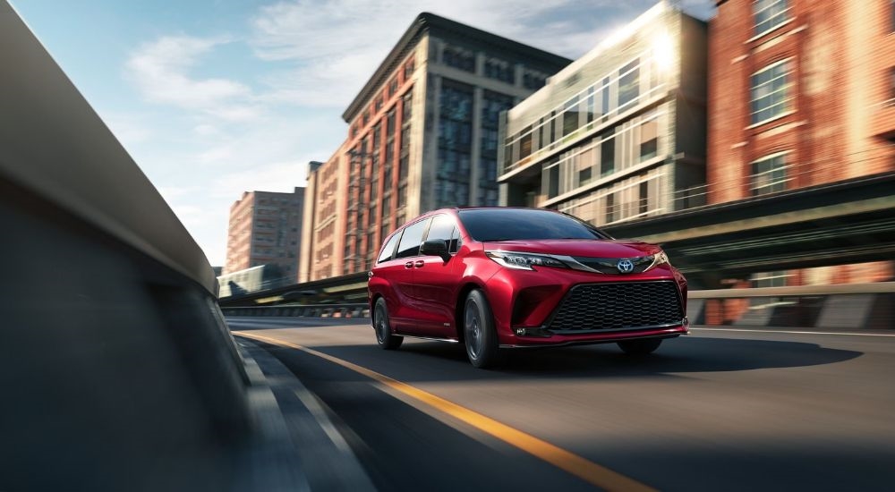 A red 2021 used Toyota Sienna for sale driving past buildings