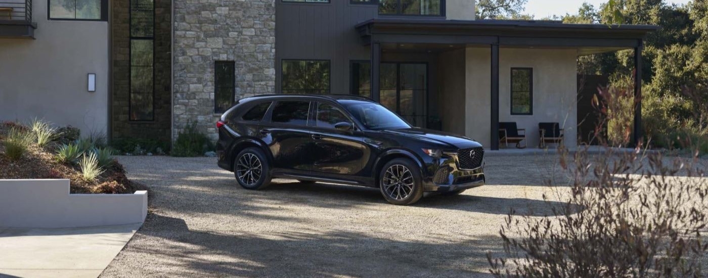 A black 2025 Mazda CX-70 parked in front of a Mazda dealer near Kendall.