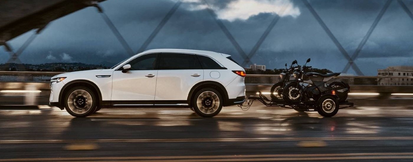 Side view of a white 2024 Mazda CX-90 towing motorcycles over a bridge.