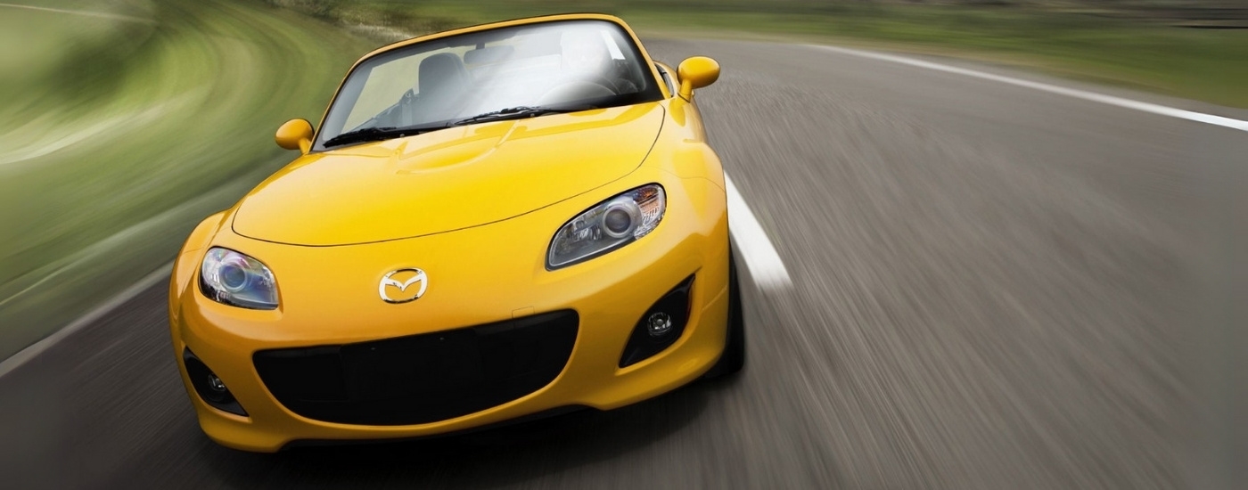 A yellow 2009 Mazda MX-5 Miata is driving to a Mazda Dealer in Miami.