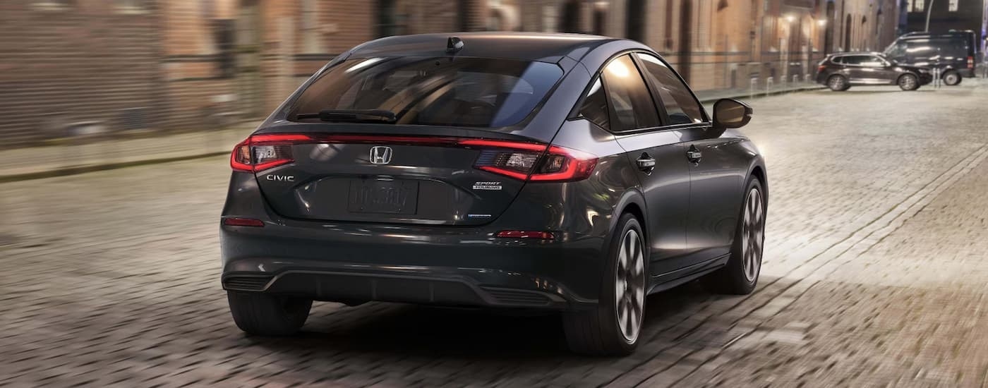 Rear view of a black 2025 Honda Civic Sport Touring Hybrid driving through a city.