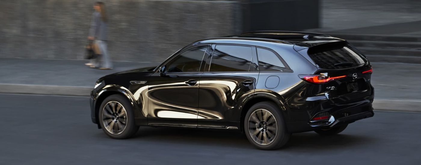 Rear view of a black 2025 Mazda CX-70 driving by a curb.