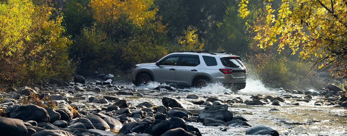 Rear view of a silver 2023 Honda Pilot driving through a shallow river.