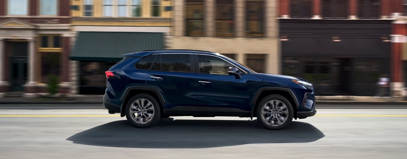 A dark blue 2025 Toyota RAV4 for sale near Greenfield driving past buildings.