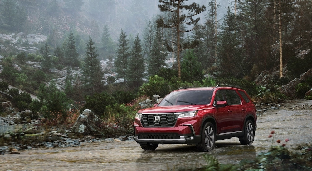 A red 2025 Honda Pilot Elite parked off-road near a forest.