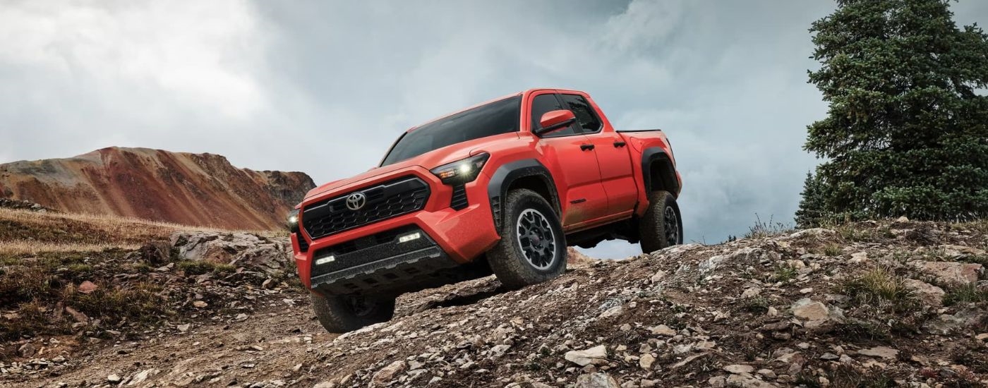 A red 2024 Toyota Tacoma TRD Off-Road driving down a dirt hill.