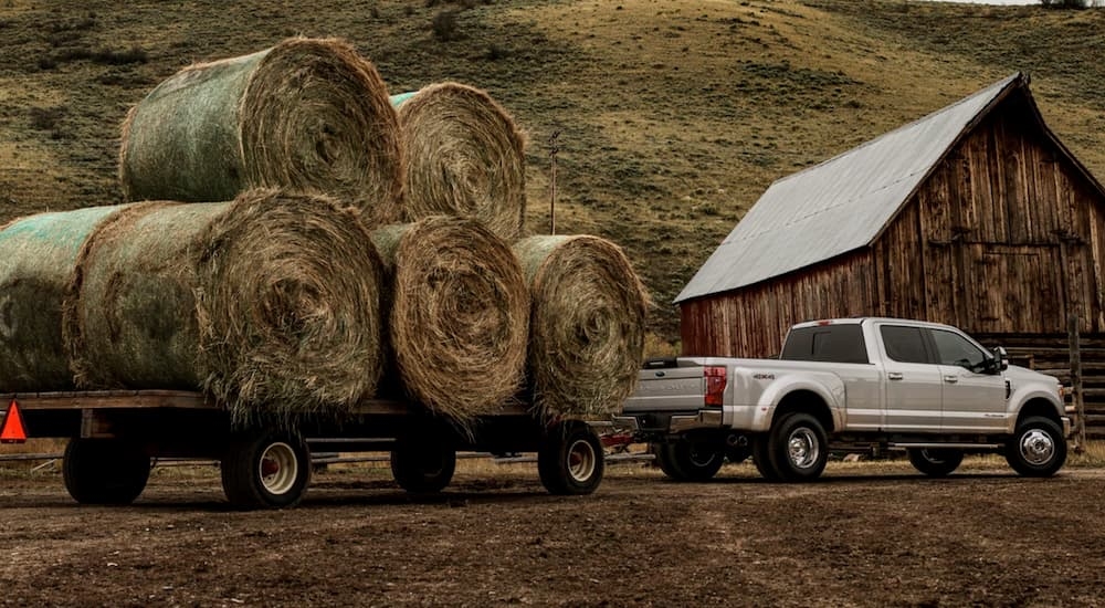 A white 2021 Ford F-350 towing a cart of hay bales.
