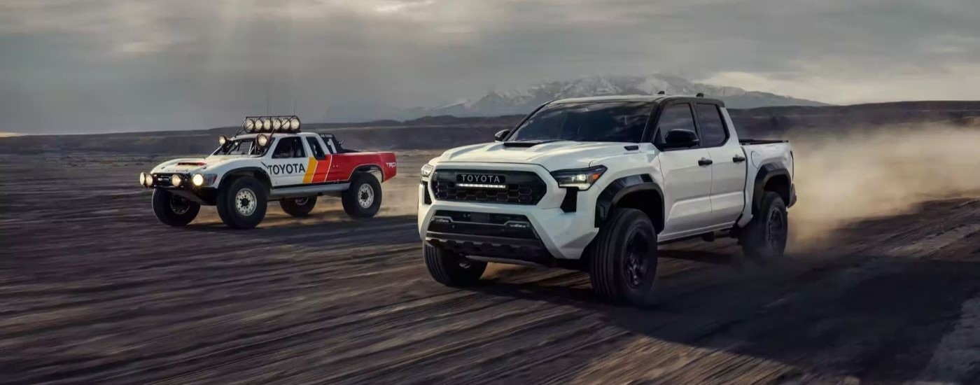 White 2024 Toyota Tacoma TRD Pro driving off-road alongside a buggy.