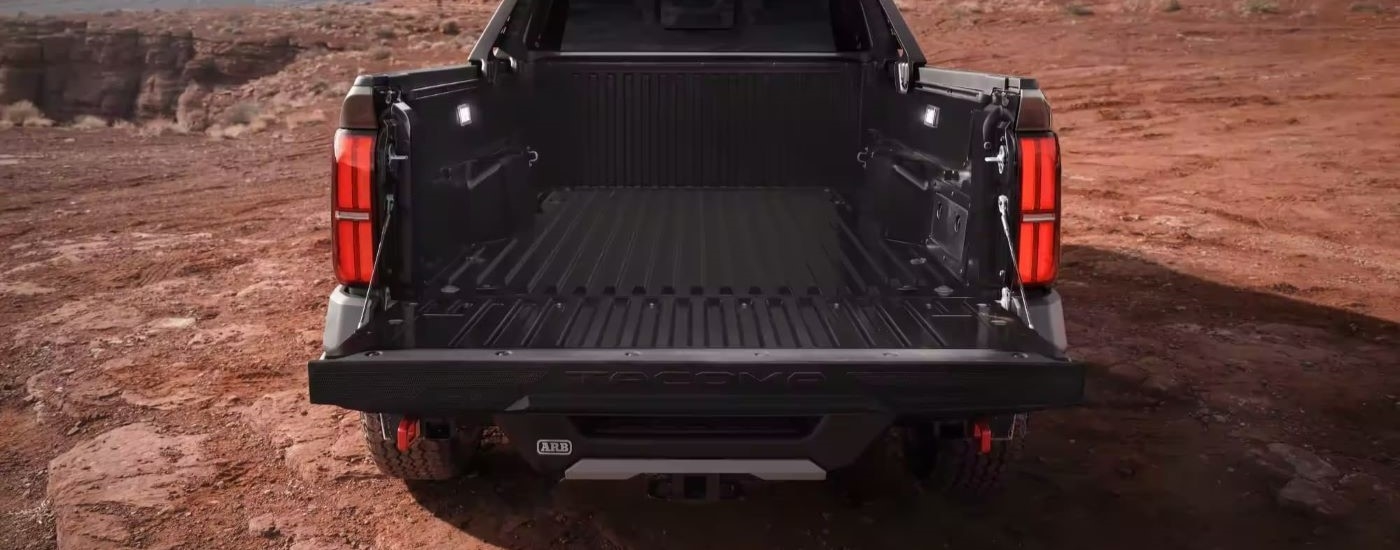 Open tailgate of a black 2024 Toyota Tacoma Trailhunter parked off-road.
