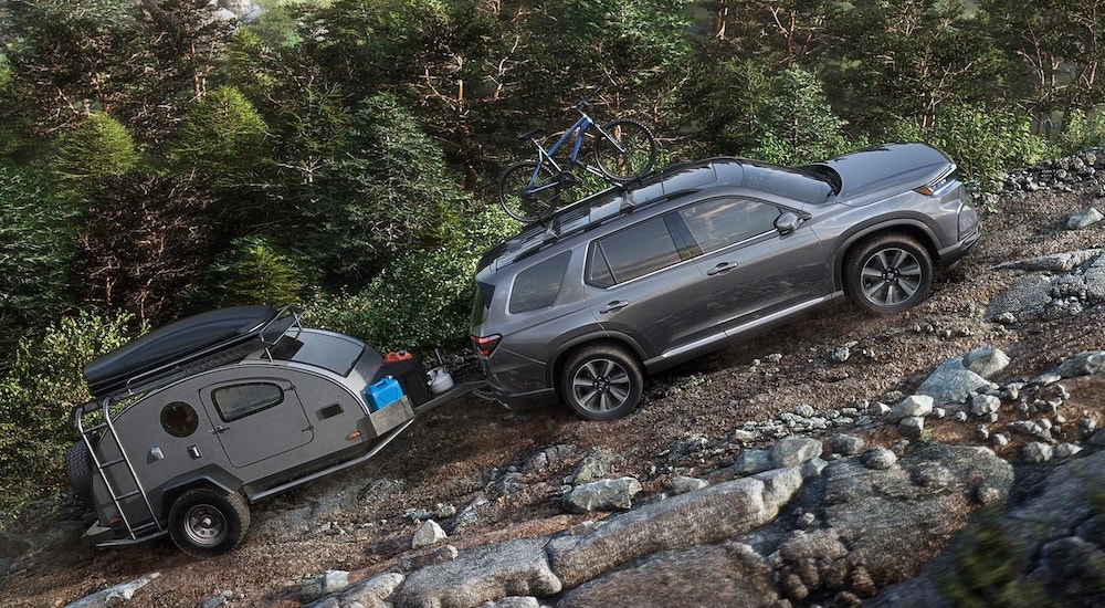 Grey 2025 Honda Pilot Sport towing a trailer up a dirt hill.
