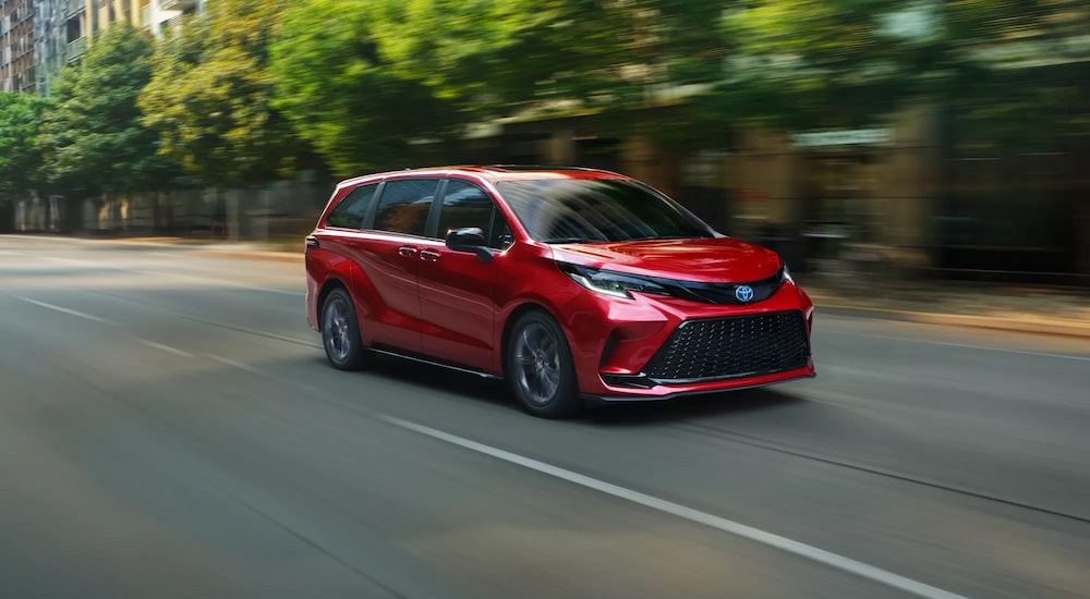 Red 2025 Toyota Sienna driving down a city road.
